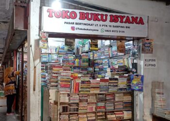 Penjual toko buku bekas, Vivi sedang merapikan buku-buku bekas tokonya di gedung oranye lantai dua Pasar Raya Padang, Minggu (2/4/2023) (Aisyah Luthfi/Genta Andalas)