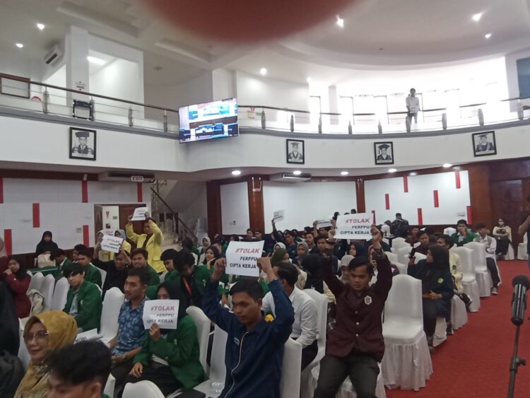 Sejumlah mahasiswa melakukan aksi angkat kertas sebagai sikap penolakan terhadap UU Cipta Kerja dalam Acara Workshop yang diadakan Satgas UU Cipta Kerja di Gedung Convention Hall UNAND pada Selasa ( 27/6/2023). ( Genta Andalas / Juniverman Yoga)